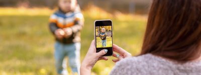 mom takes pictures of her baby on a smartphone in an autumn park